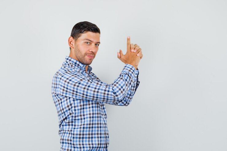 Foto gratuito macho joven haciendo gesto de disparo en camisa a cuadros y mirando alegre