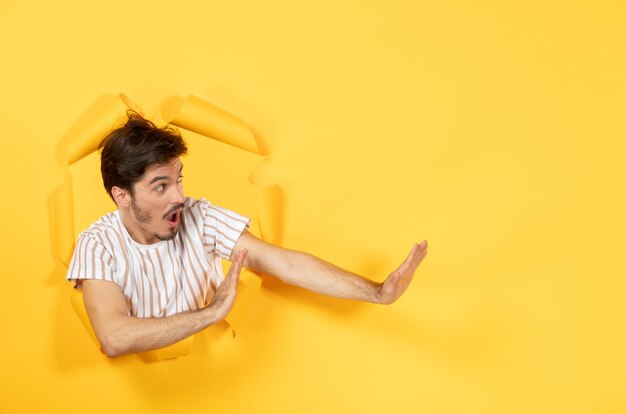 Macho joven mirando desde el fondo de papel amarillo rasgado chico facial interior