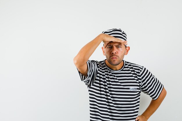 Macho joven mirando lejos con las manos sobre la cabeza en el sombrero de camiseta a rayas