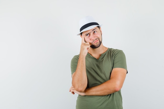 Macho joven mirando a otro lado en camiseta verde y sombrero y mirando pensativo