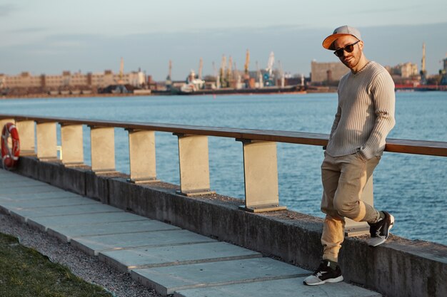 Macho joven de moda en gafas de sol, snapback y zapatillas inclinadas