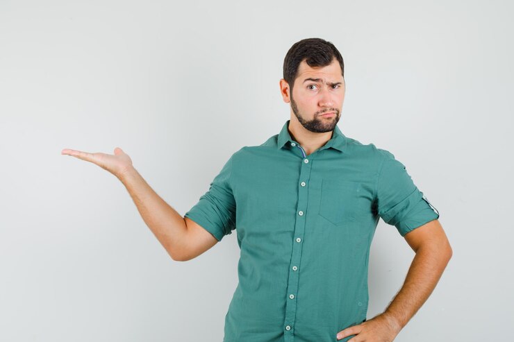 Foto gratuito macho joven mostrando la palma de la mano a un lado en camisa verde y mirando ansioso, vista frontal.