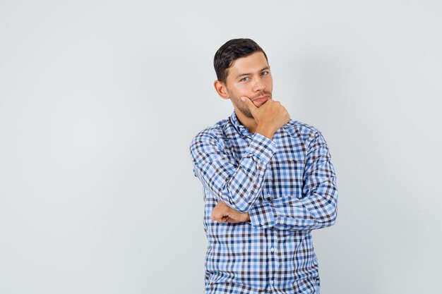 Macho joven de pie en pose de pensamiento en camisa a cuadros y mirando sensible