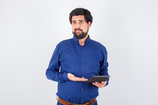 Macho joven que muestra la calculadora en camisa azul real, vista frontal.