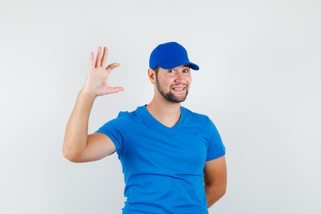 Macho joven que muestra un cartel de tamaño pequeño en camiseta azul y gorra y mirando alegre