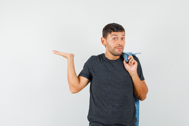 Foto gratuita macho joven sosteniendo la chaqueta en la espalda extendiendo la palma a un lado en camiseta y mirando alegre