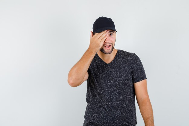 Macho joven sosteniendo la mano en un ojo en camiseta y gorra