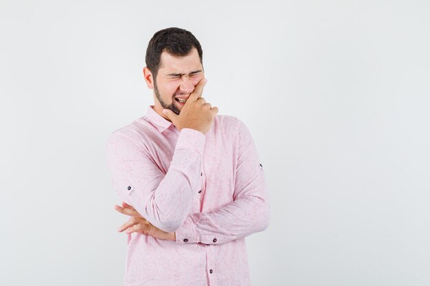 Macho joven sosteniendo su barbilla mientras se ríe en camisa rosa