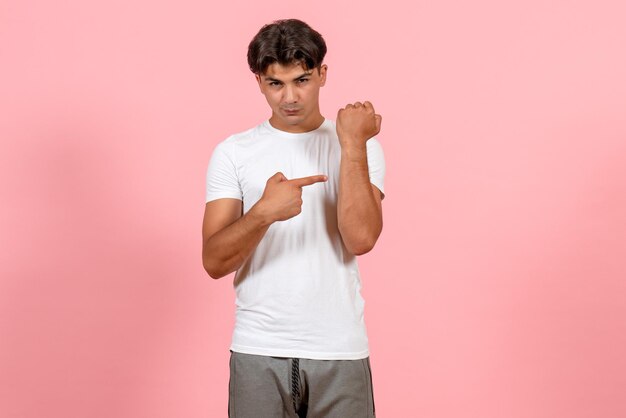 Macho joven de vista frontal apuntando su mano en camiseta blanca sobre fondo rosa