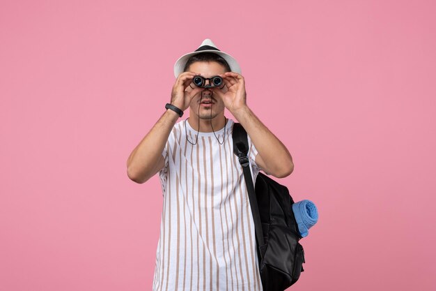 Macho joven de vista frontal con bolsa y binoculares en el fondo de color rosa