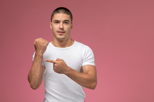 Macho joven de vista frontal con camisa blanca mostrando su muñeca sobre el fondo rosa