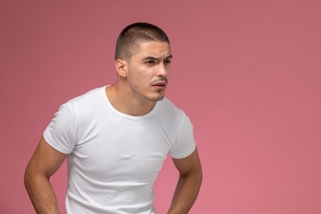 Macho joven de vista frontal en camiseta blanca mirando a lo lejos sobre fondo rosa