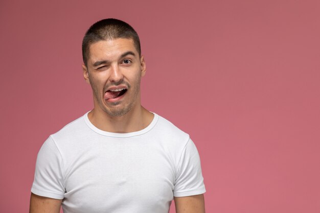 Macho joven de vista frontal en camiseta blanca mostrando su lengua sobre fondo rosa