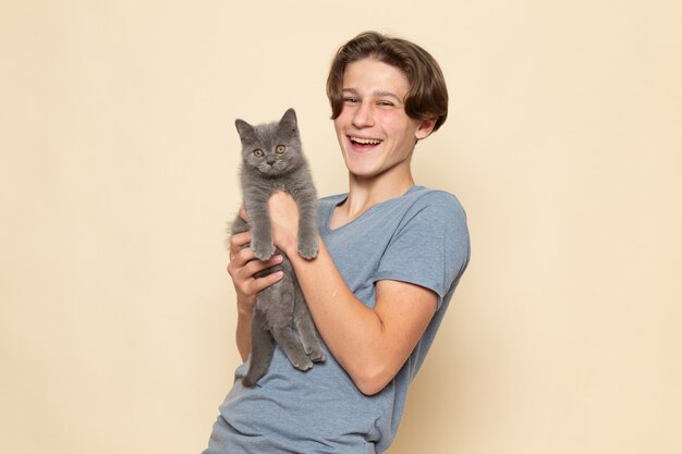 Un macho joven de vista frontal en camiseta gris posando con risa sosteniendo lindo gatito gris