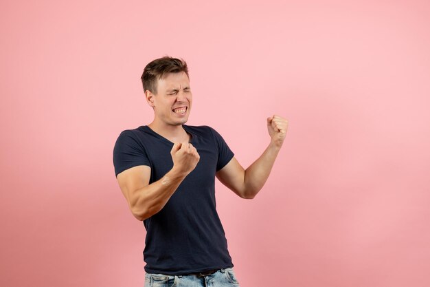 Macho joven de vista frontal en camiseta oscura posando regocijo sobre fondo rosa