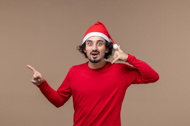 Macho joven de vista frontal con capa roja de navidad sobre fondo marrón oscuro emoción vacaciones navidad