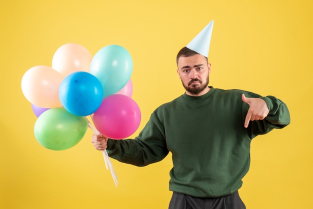 Macho joven de vista frontal con globos de colores sobre fondo amarillo