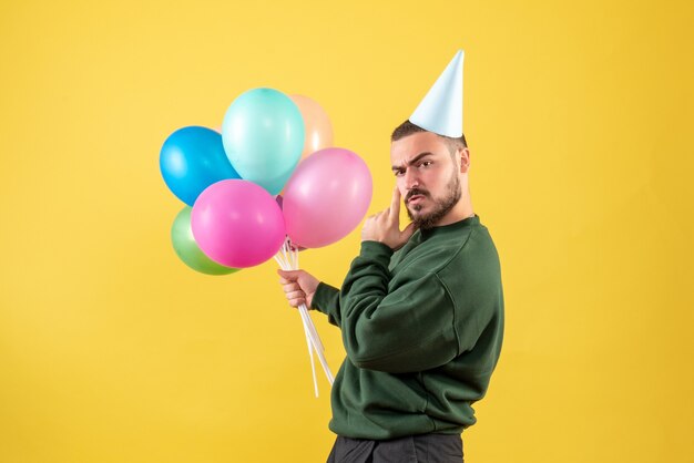 Macho joven de vista frontal con globos de colores sobre fondo amarillo