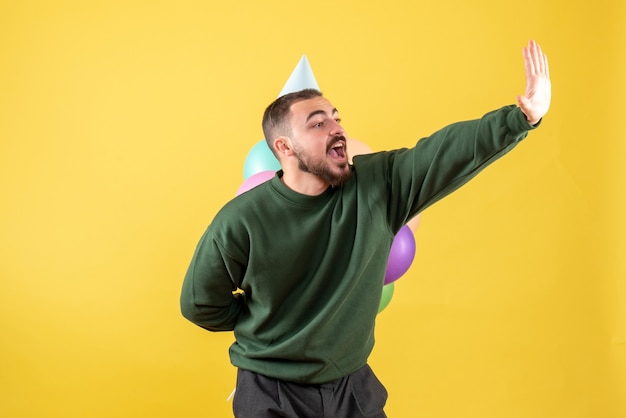 Macho joven de vista frontal con globos de colores sobre fondo amarillo