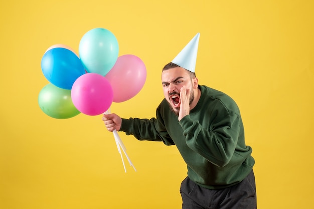 Macho joven de vista frontal con globos de colores sobre fondo amarillo