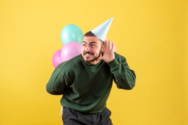 Macho joven de vista frontal con globos de colores sobre fondo amarillo