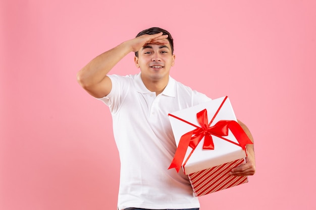 Macho joven de vista frontal con gran regalo de Navidad mirando a distancia sobre fondo rosa