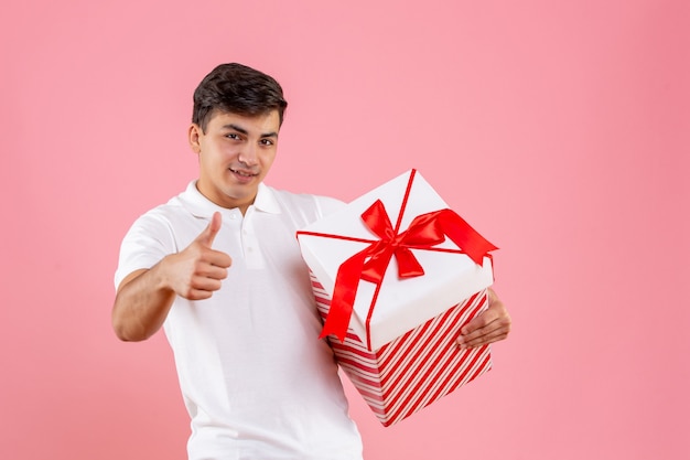 Macho joven de vista frontal con gran regalo de Navidad sobre fondo rosa