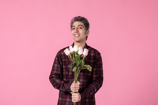 Macho joven de vista frontal con hermosas rosas rosadas en la pared rosa