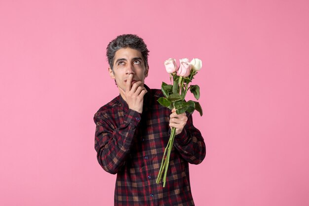 Macho joven de vista frontal con hermosas rosas rosadas en la pared rosa