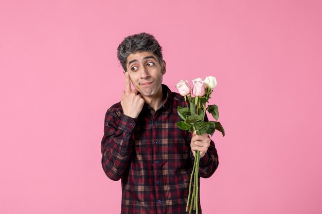 Macho joven de vista frontal con hermosas rosas rosadas en la pared rosa