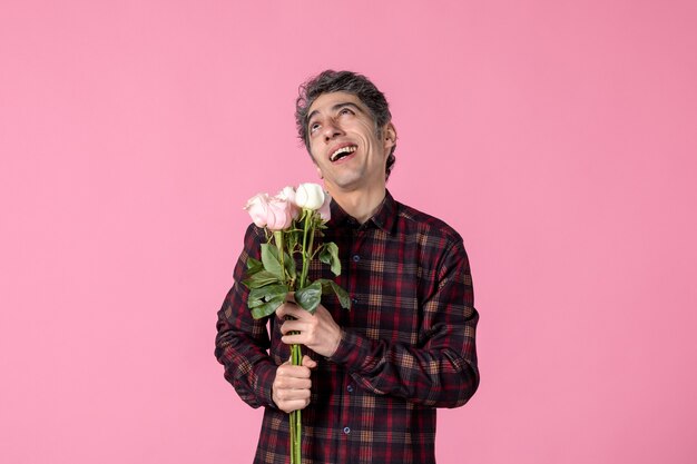 Macho joven de vista frontal con hermosas rosas rosadas en la pared rosa