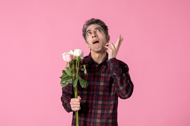 Macho joven de vista frontal con hermosas rosas rosadas en la pared rosa