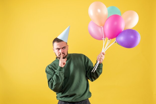 Macho joven de vista frontal sosteniendo globos de colores sobre un fondo amarillo