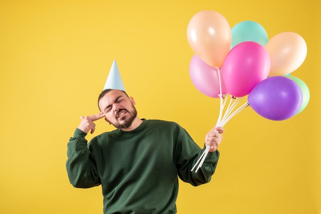 Macho joven de vista frontal sosteniendo globos de colores sobre un fondo amarillo