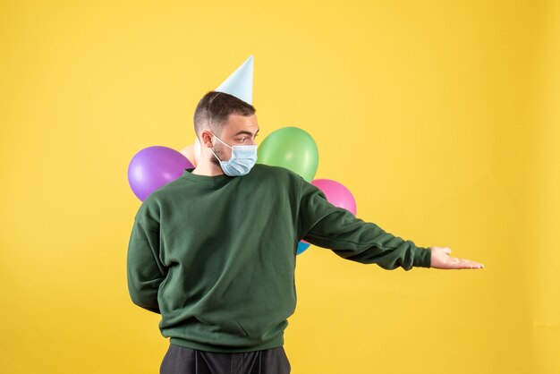 Macho joven de vista frontal sosteniendo globos de colores sobre un fondo amarillo