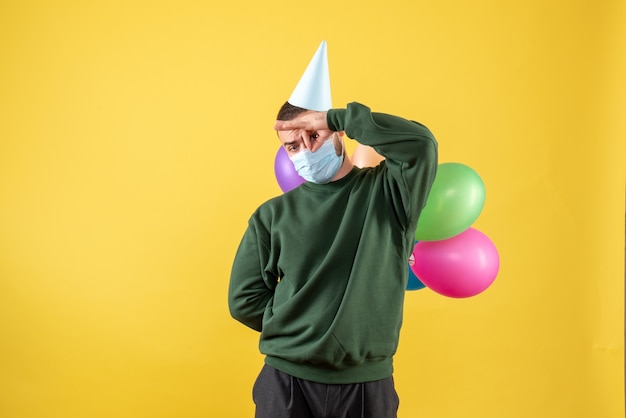 Macho joven de vista frontal sosteniendo globos de colores sobre un fondo amarillo