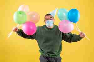 Foto gratuita macho joven de vista frontal sosteniendo globos de colores sobre un fondo amarillo