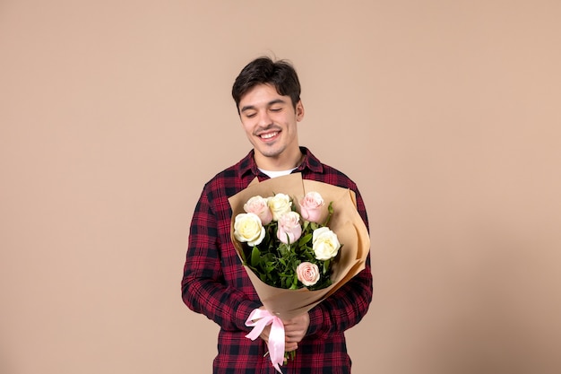 Macho joven de vista frontal sosteniendo hermosas flores en la pared marrón