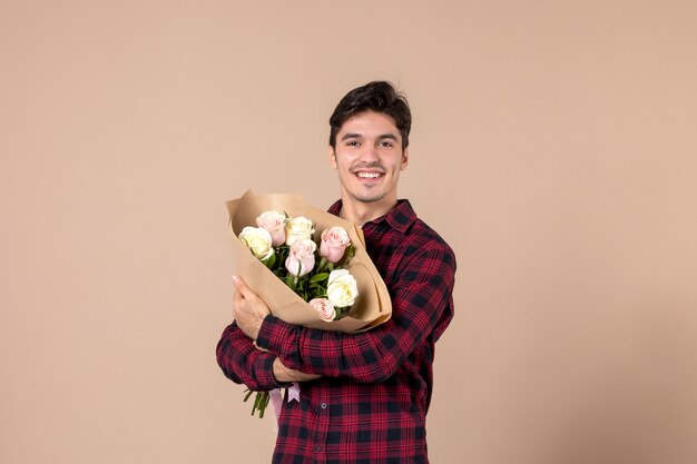 Macho joven de vista frontal sosteniendo hermosas flores en la pared marrón