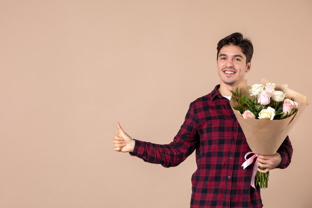 Macho joven de vista frontal sosteniendo hermosas flores en la pared marrón