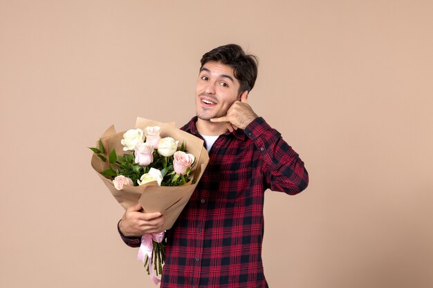 Macho joven de vista frontal sosteniendo hermosas flores en la pared marrón