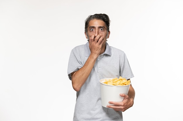 Macho joven de vista frontal sosteniendo papas fritas y viendo la película en un escritorio blanco