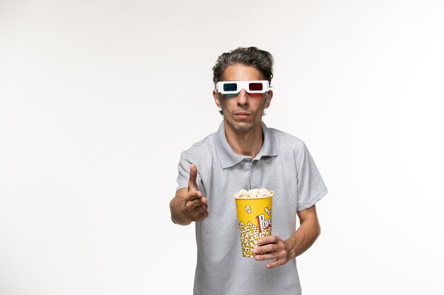 Macho joven de vista frontal sosteniendo el paquete de palomitas de maíz en d gafas de sol agitando las manos sobre una superficie blanca