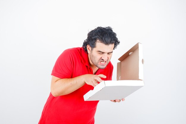 Macho maduro mirando caja de pizza abierta en camiseta roja y mirando hambriento. vista frontal.