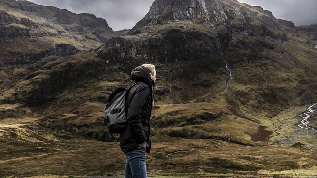 Macho en una mochila y un abrigo cálido caminando en las tierras altas de Escocia bajo un cielo gris