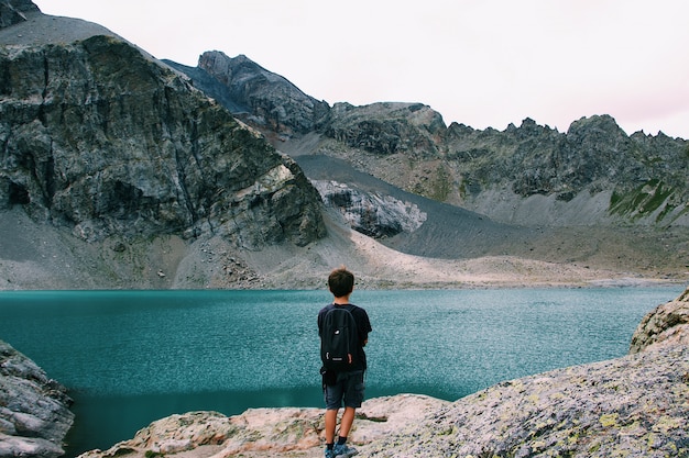 Macho con una mochila de pie en un acantilado disfrutando de la vista del mar cerca de una montaña