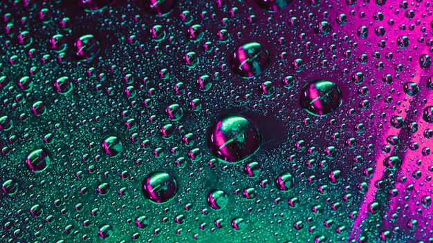 Foto gratuita macro de gotas de agua verde y rosa en la superficie