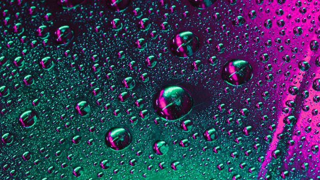 Macro de gotas de agua verde y rosa en la superficie