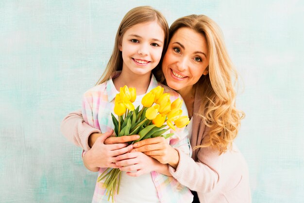 Madre abrazando hija y sosteniendo tulipanes