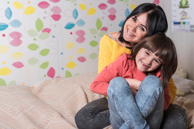 Madre abrazando a su hija por detrás en la cama